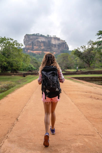 Female backpacker walking towards Sigiriya rock temple in Sri Lanka carrying her bag - travel concepts